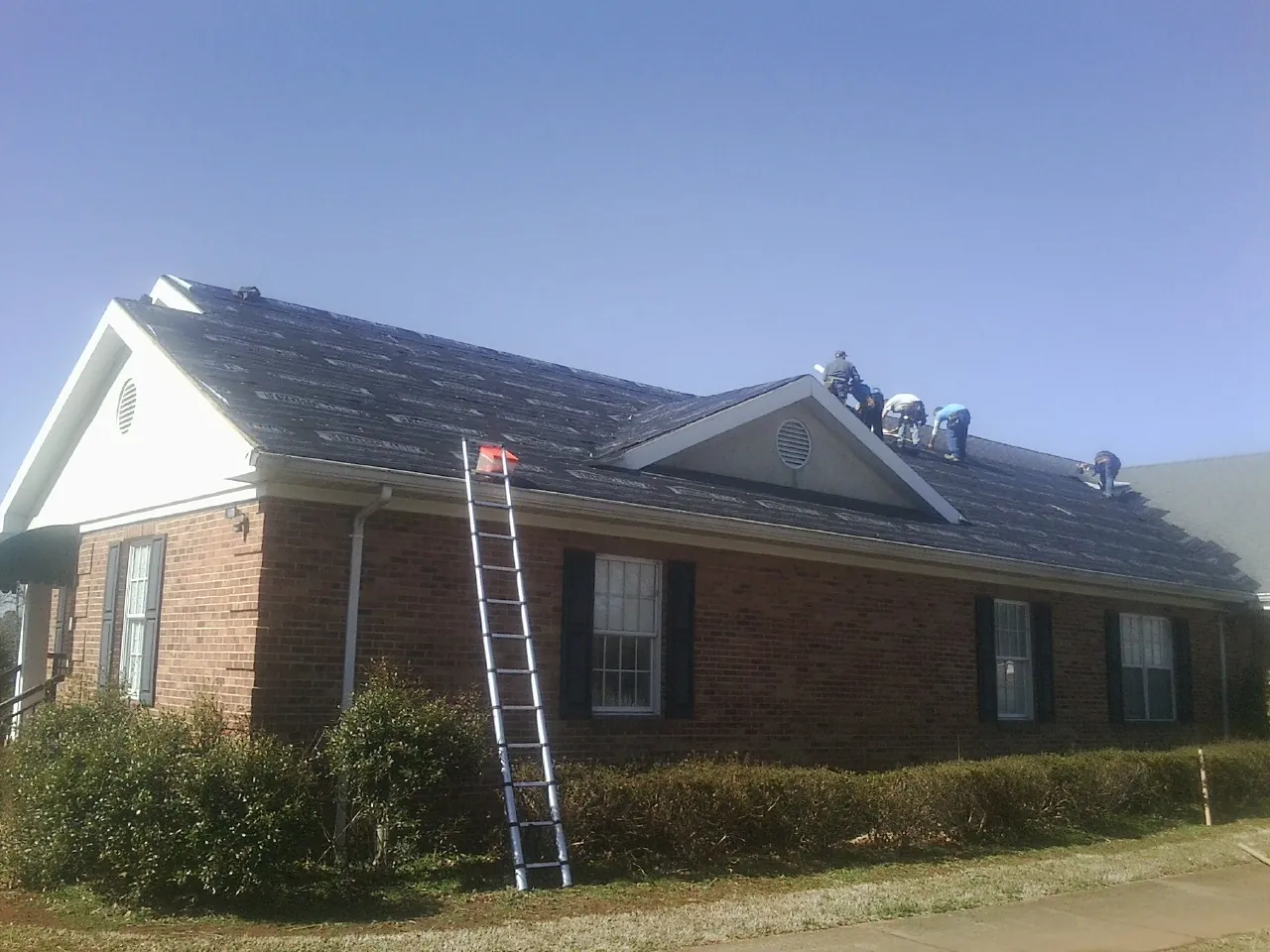 Crew tearing shingles off a brick ranch roof with a ladder set — Emergency Roof Repair work by our crew in Pescadero
