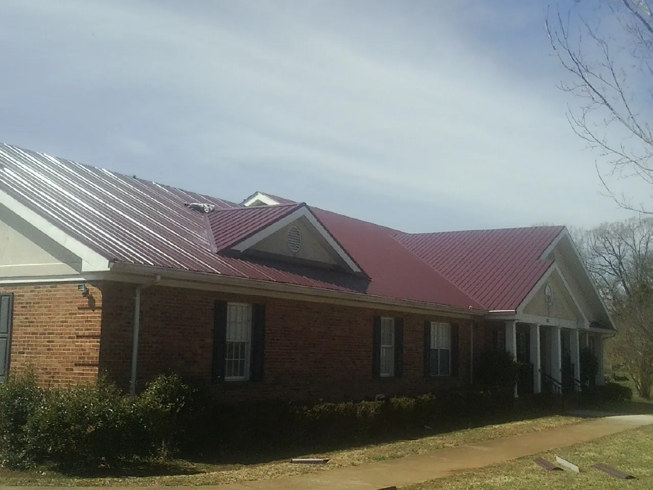 Red metal roof with gabled entries on a long brick building, from a Hail Damage Roof Repair job in Pescadero