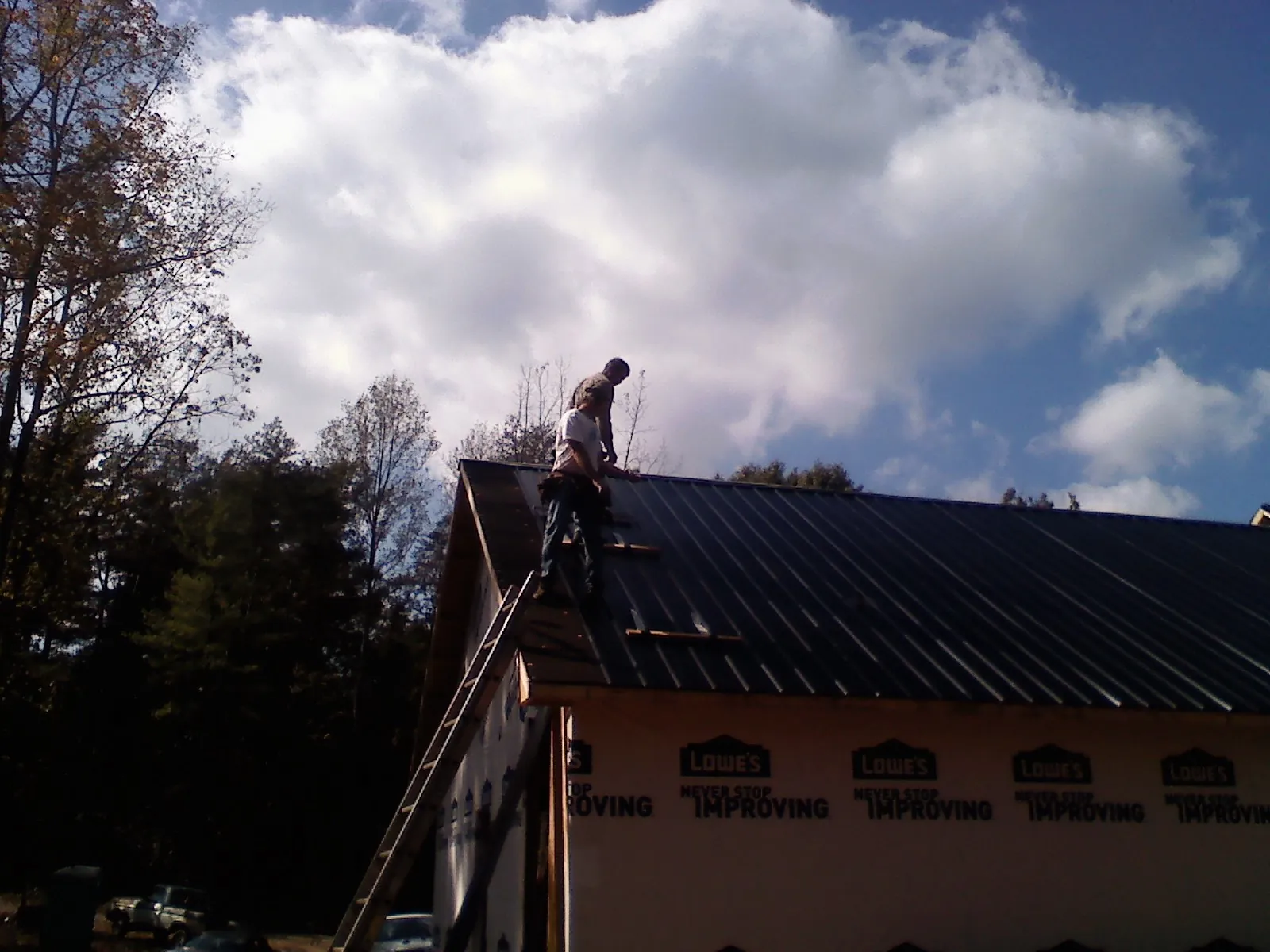 Roofer fastening dark metal panels high against a cloudy sky, from a Roof Inspection job in Pescadero
