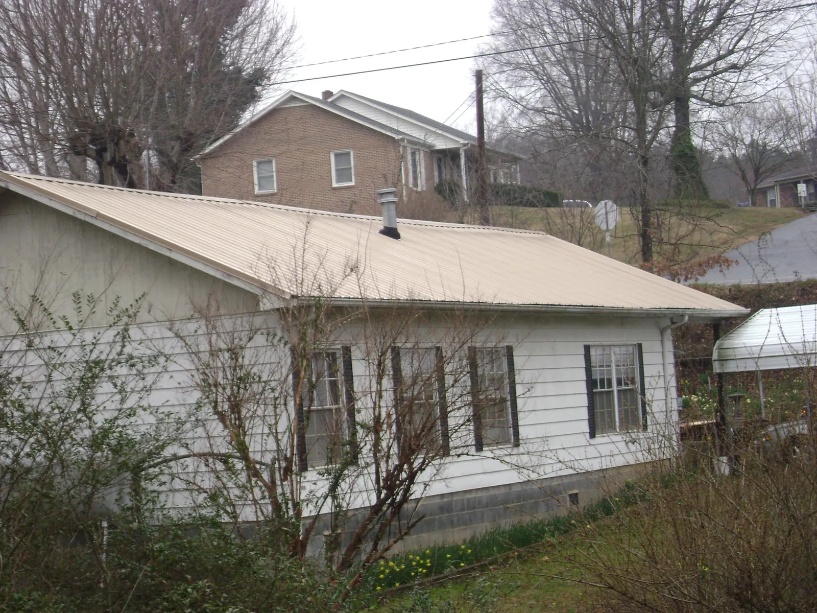 Tan metal roof on a white sided house set into a hillside — Commercial Roofing by Roofing Brothers in Pescadero